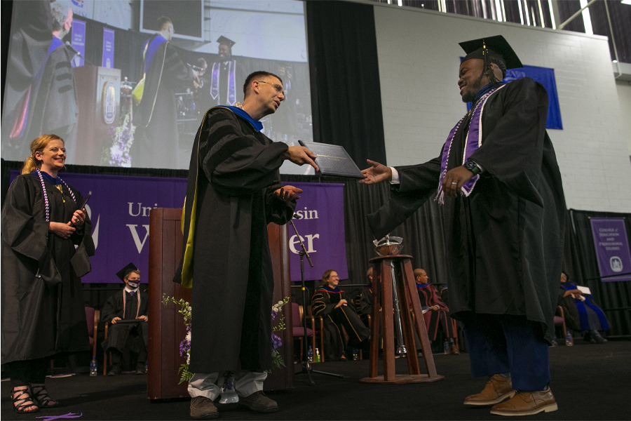 Matt Vick stands on the stage at graduation, hands a diploma to a student crossing the stage.